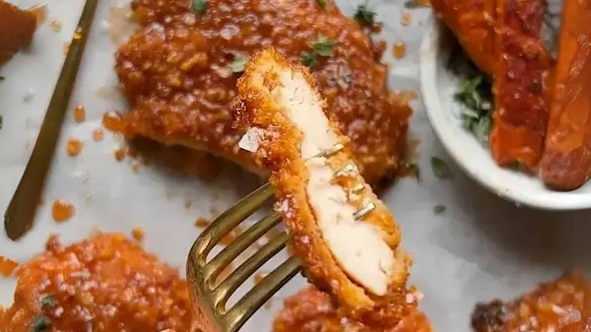 Close-up of a sliced hot honey chicken tender on a fork showing crispy crust and juicy interior