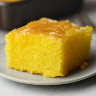 A Lemon Cake to Die for! 9 Close-up of a moist, vibrant yellow slice of A Lemon Cake to Die for! with a glossy lemon glaze, served on a white plate.
