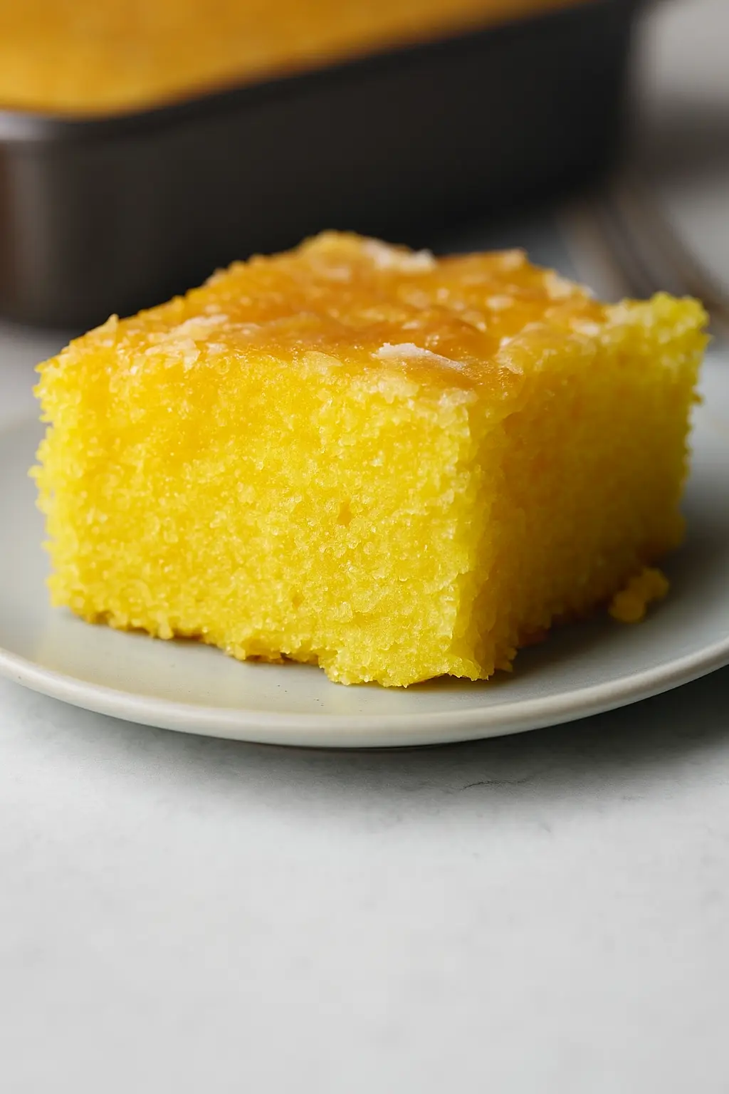 A Lemon Cake to Die for! 6 Close-up of a moist, vibrant yellow slice of A Lemon Cake to Die for! with a glossy lemon glaze, served on a white plate.