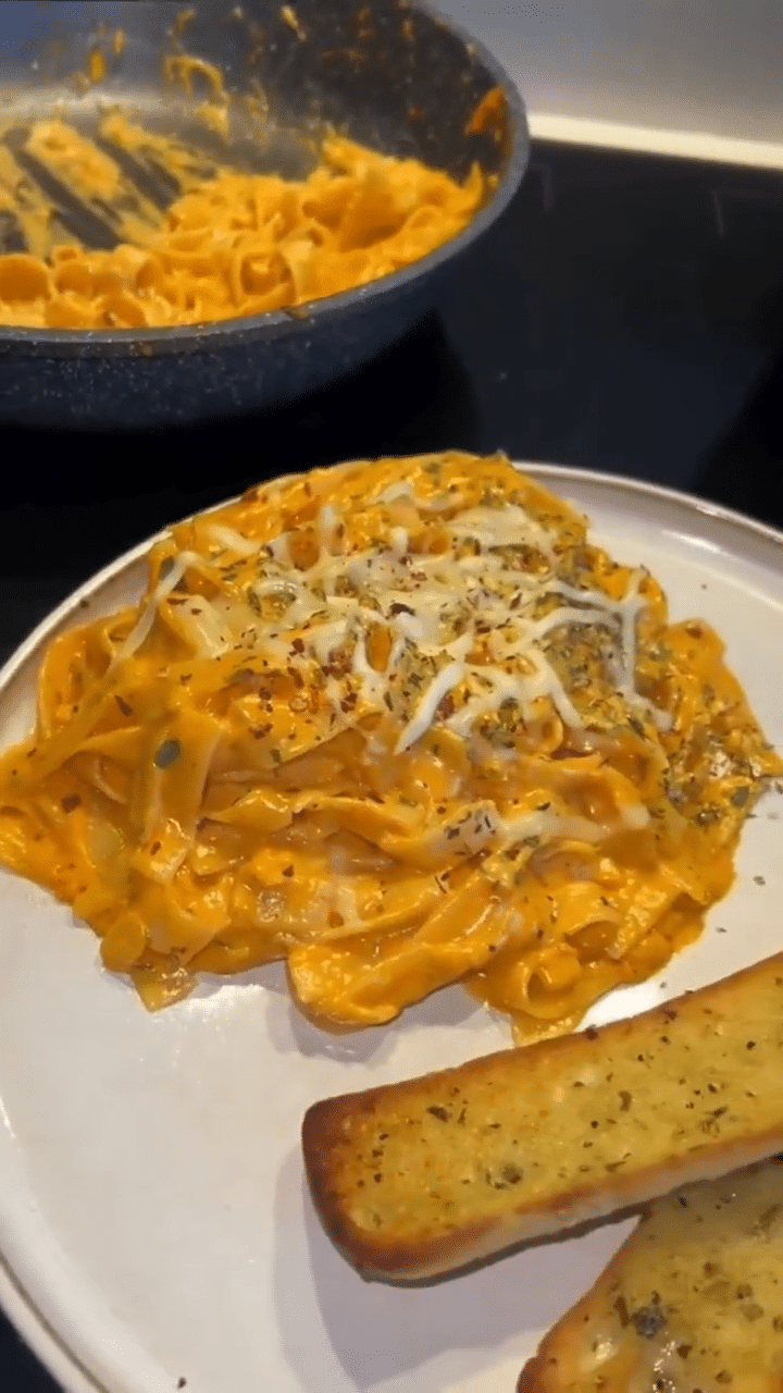 Cooking process close-up: Tagliatelle being tossed in a shallow stainless-steel skillet with a silky